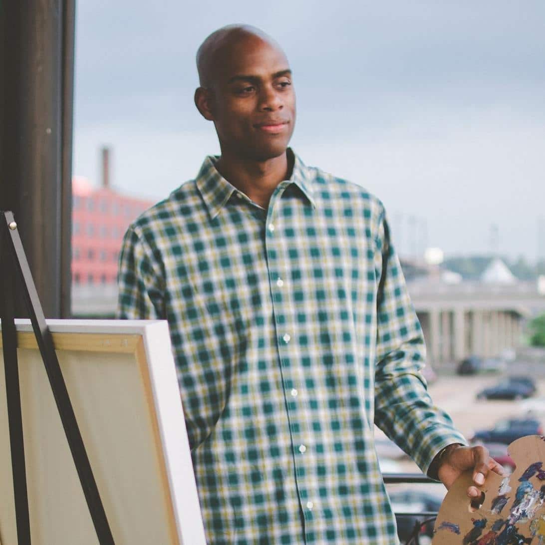 Portrait of Nashville-based painter Omari Booker standing at his easel while holding a painter's palette.